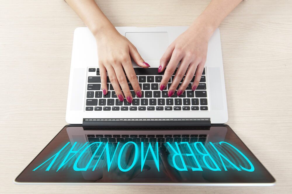 Imagem de um notebook, visto de cima, no qual uma pessoa está digitando. Na tela é possível notar que está escrito a frase "Cyber Monday".