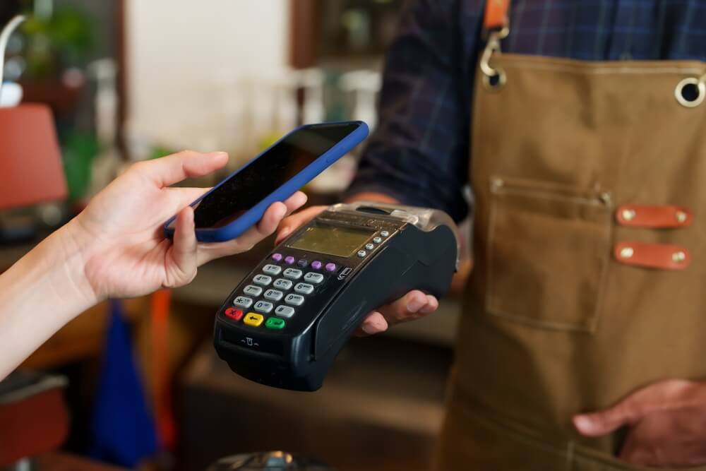 Uma pessoa pagando via cashback em uma maquininha de cartão utilizando o celular.