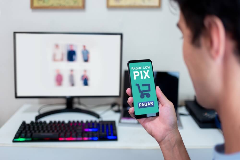 Imagem de uma pessoa com o celular na mão. Ela está utilizando o PIX para finalizar uma compra em um e-commerce.