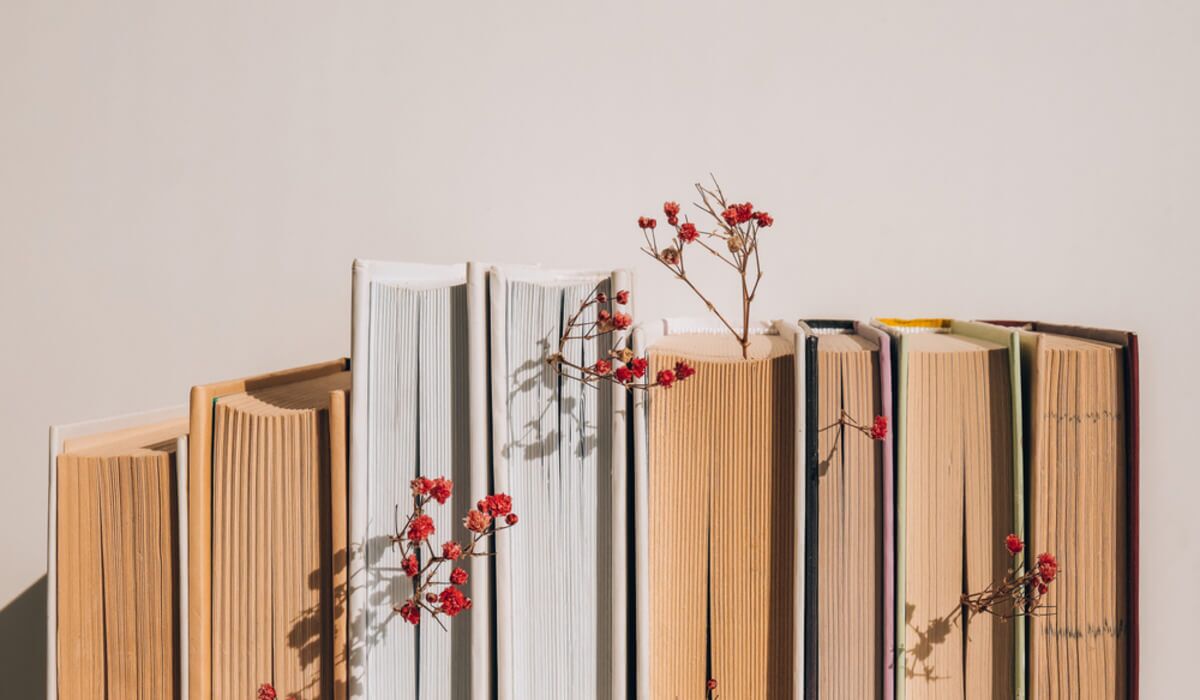 Imagem Da Lombada De Alguns Livros. No Meio Deles, é Possível Ver Alguns Ramos De Flores.