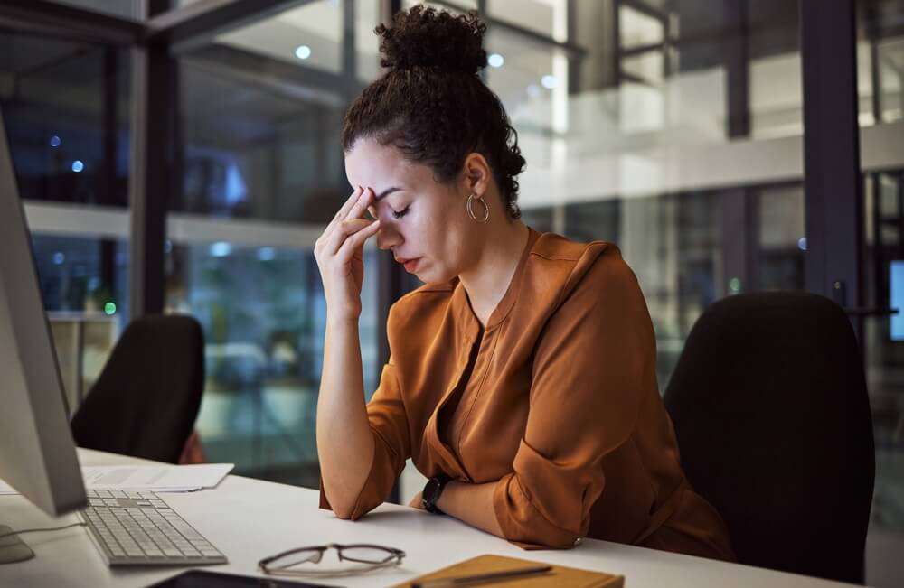Imagem de uma mulher. Ela está no trabalho e aparenta estar estressada, cansada.